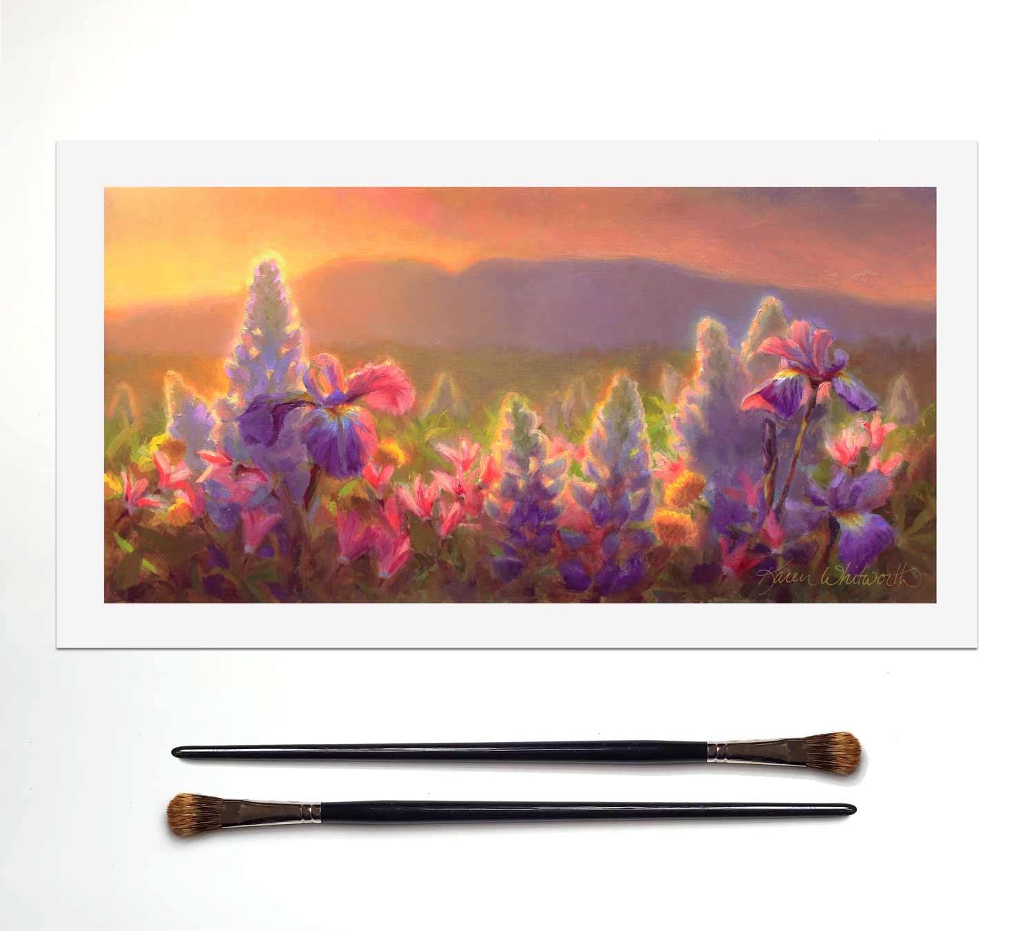 Sleeping Lady Alaska wall art mountain landscape painting of wildflowers and Mt Susitna. The artwork is sitting on a white table next to 2 paintbrushes.
