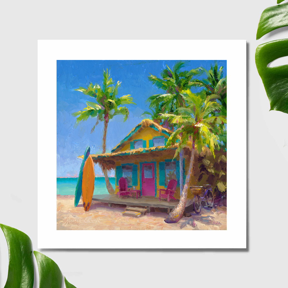 Surf wall art print painting of beach shack with surf boards. The paper print is sitting on a white table with tropical green leaves.