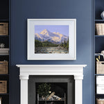 Alaska art print of Denali mountain wall art in a nature landscape painting. The artwork is displayed in a white wood picture frame over a fireplace mantel on a dark blue wall.