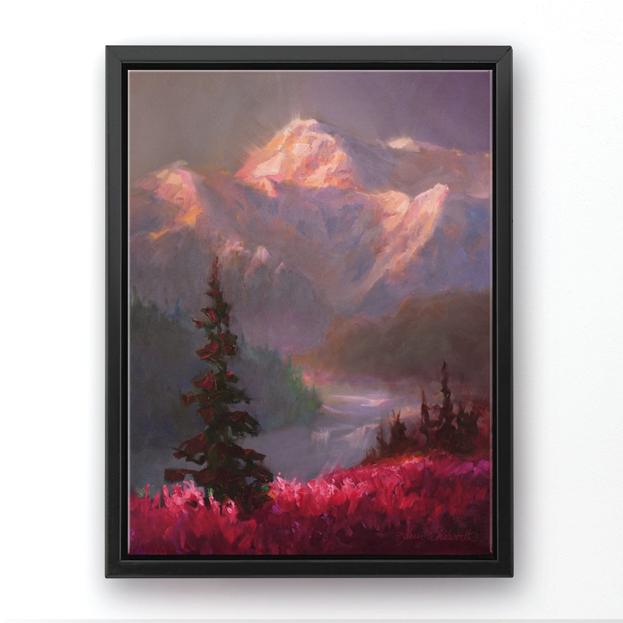 Alaska canvas art of mountain landscape painting depicting Denali in the background and trees and fireweed flowers in the foreground. The wall art is framed in a black floater frame and hanging on a white wall.