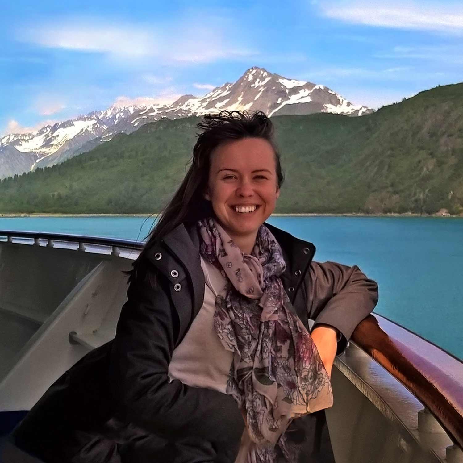 Alaska artist Karen Whitworth standing in front of scenery of a coastal mountain landscape.