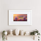 Framed wildflower wall art print featuring a flower field landscape painting of Sleeping Lady Mountain, also known as Mt Susitna, in Southcentral Alaska. The artwork is framed in a white picture frame made of wood, and is hanging on a beige wall. above a farmhouse decor themed shelf and vases.