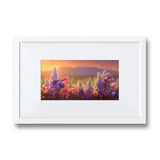 Framed wildflower wall art print featuring a flower field landscape painting of Sleeping Lady Mountain, also known as Mt Susitna, in Southcentral Alaska. The artwork is framed in a white picture frame made of wood, and is hanging on a white wall.