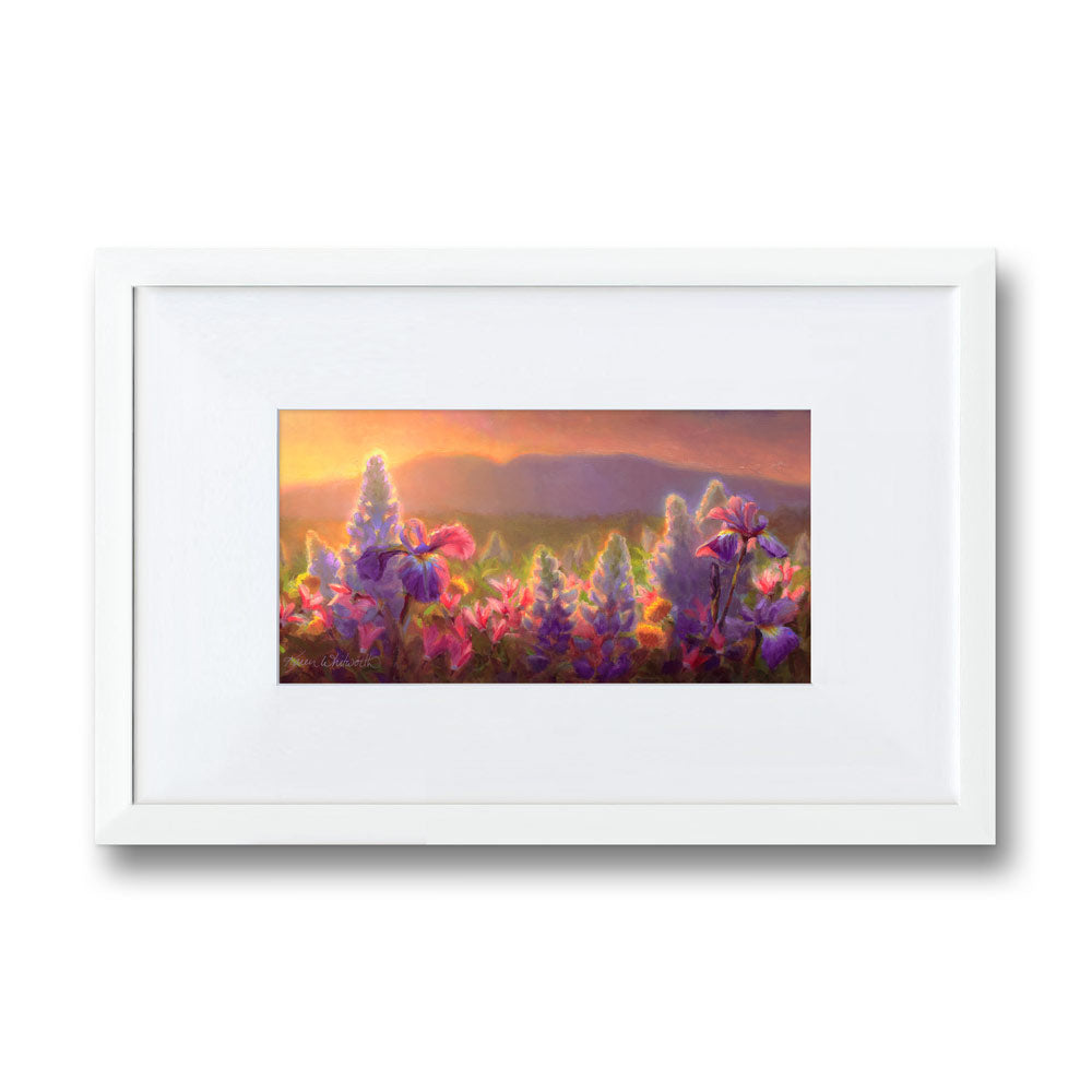 Framed wildflower wall art print featuring a flower field landscape painting of Sleeping Lady Mountain, also known as Mt Susitna, in Southcentral Alaska. The artwork is framed in a white picture frame made of wood, and is hanging on a white wall.