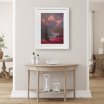 Alaska wall art print of a mountain sunset landscape painting depicting Denali and a field of fireweed wildflowers. The painting is titled "Denali Summer" by Karen Whitworth and is framed in a white wood picture frame. It is hanging on a beige wall behind a rustic farmhouse home decor table.