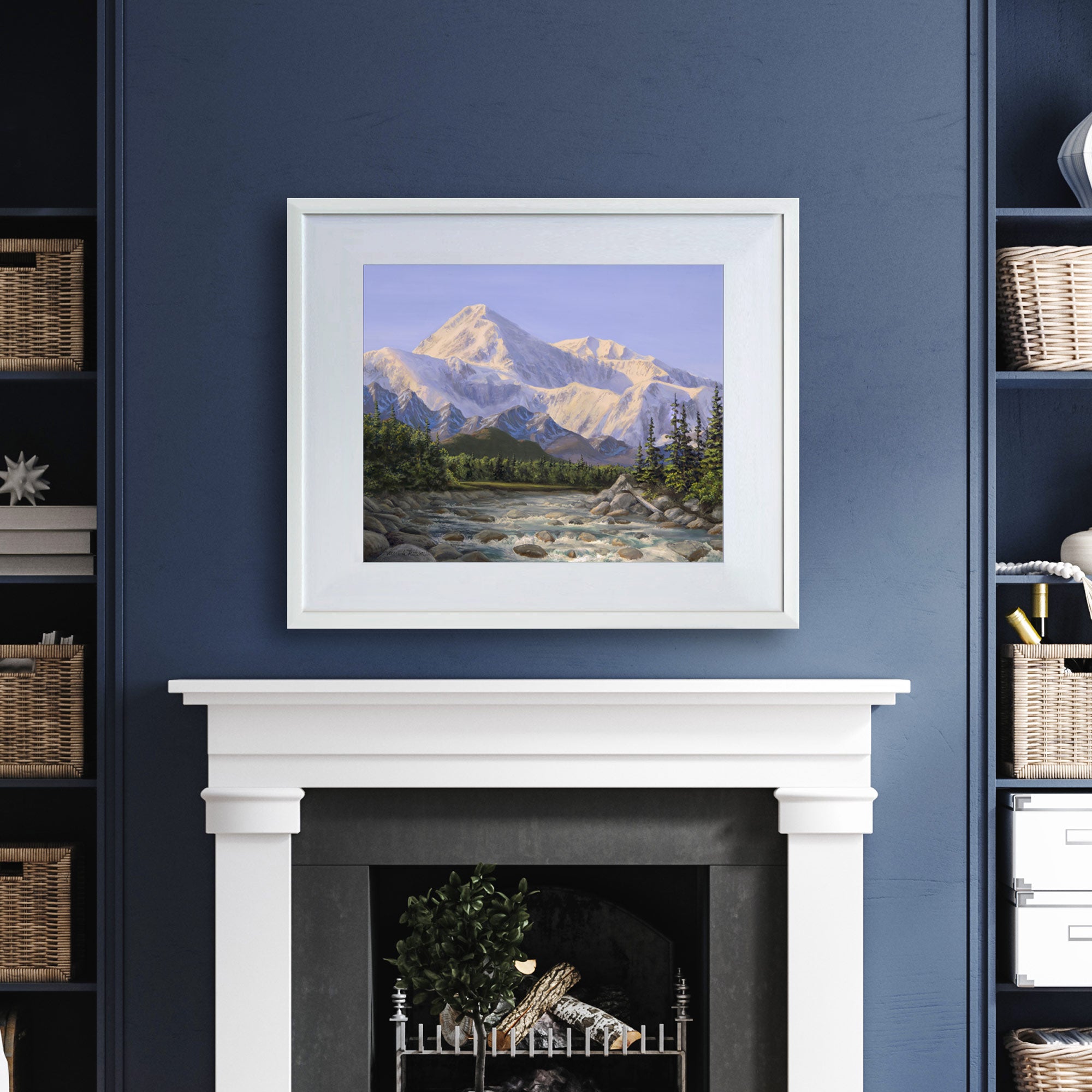 Alaska art print of Denali mountain wall art in a nature landscape painting. The artwork is displayed in a white wood picture frame over a fireplace mantel on a dark blue wall. 