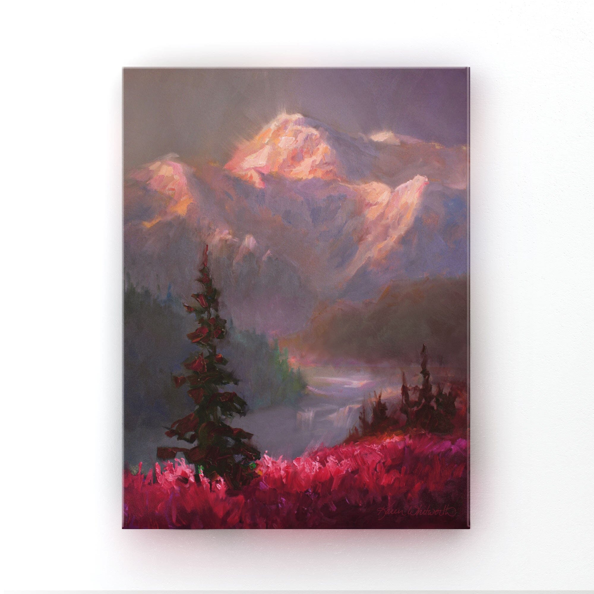 Alaska canvas art of mountain landscape painting depicting Denali in the background and trees and fireweed flowers in the foreground. The wall art is hanging on a white wall. 