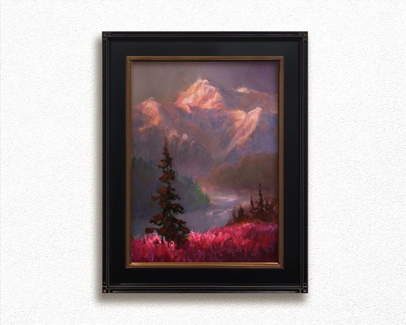 Alaska art featuring a painting of a mountain alpenglow sunset painting. The mountain landscape scene is framed and hanging on a white wall.