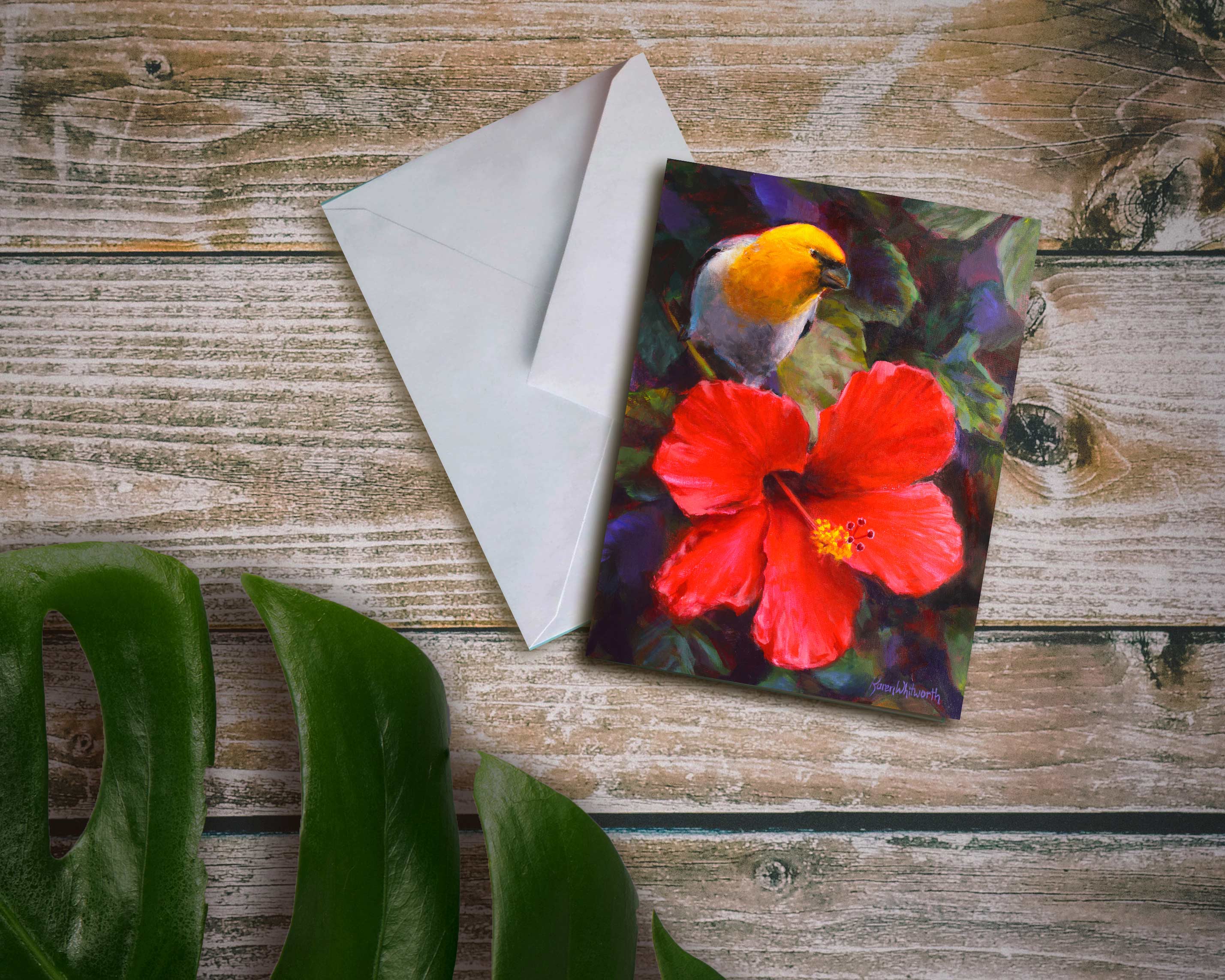 An envelope and card featuring art of a tropical Hawaiian Hibiscus flower and an endemic Palila bird on a wood background