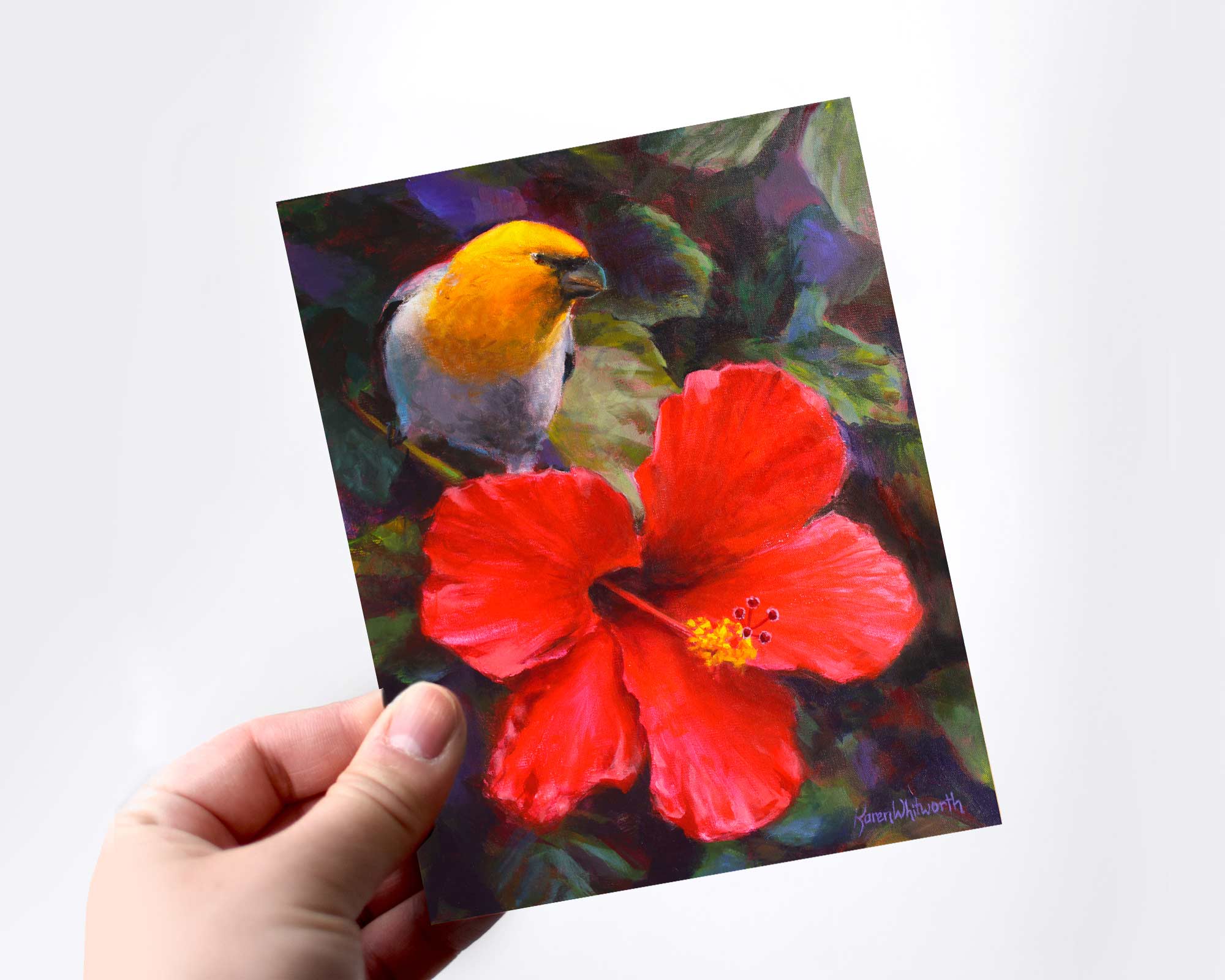 A hand holding a card featuring art of a tropical Hawaiian Hibiscus flower and an endemic Palila bird