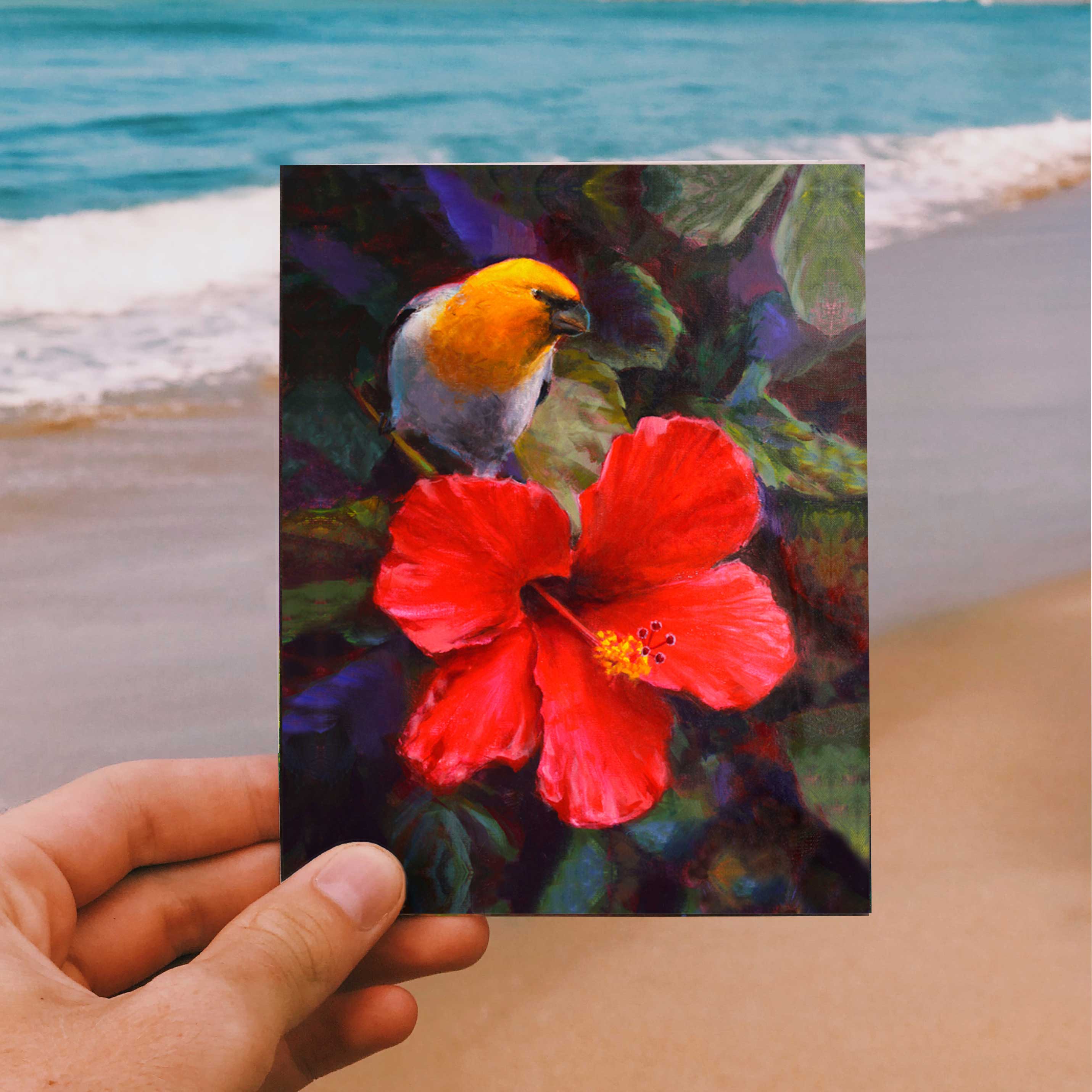 Hand holding an envelope and card featuring art of a tropical Hawaiian Hibiscus flower and an endemic Palila bird on beach background