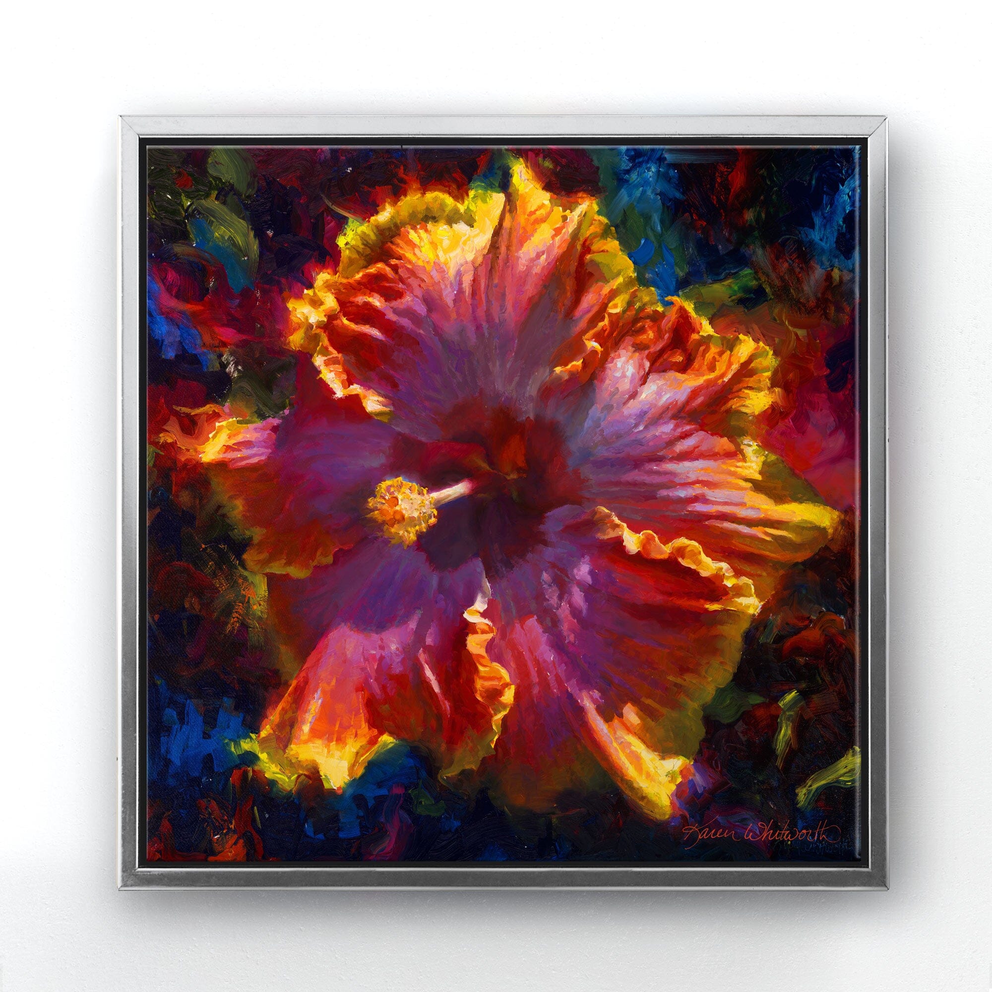 Square canvas wall art in a contemporary silver minimalist frame. The artwork is a painting by Karen Whitworth of a large Hawaiian hibiscus flower, painted in a lively impressionistic style. Vibrant colors and brushstrokes swirl around the flower in a dark background. The painting is hanging on a white wall.