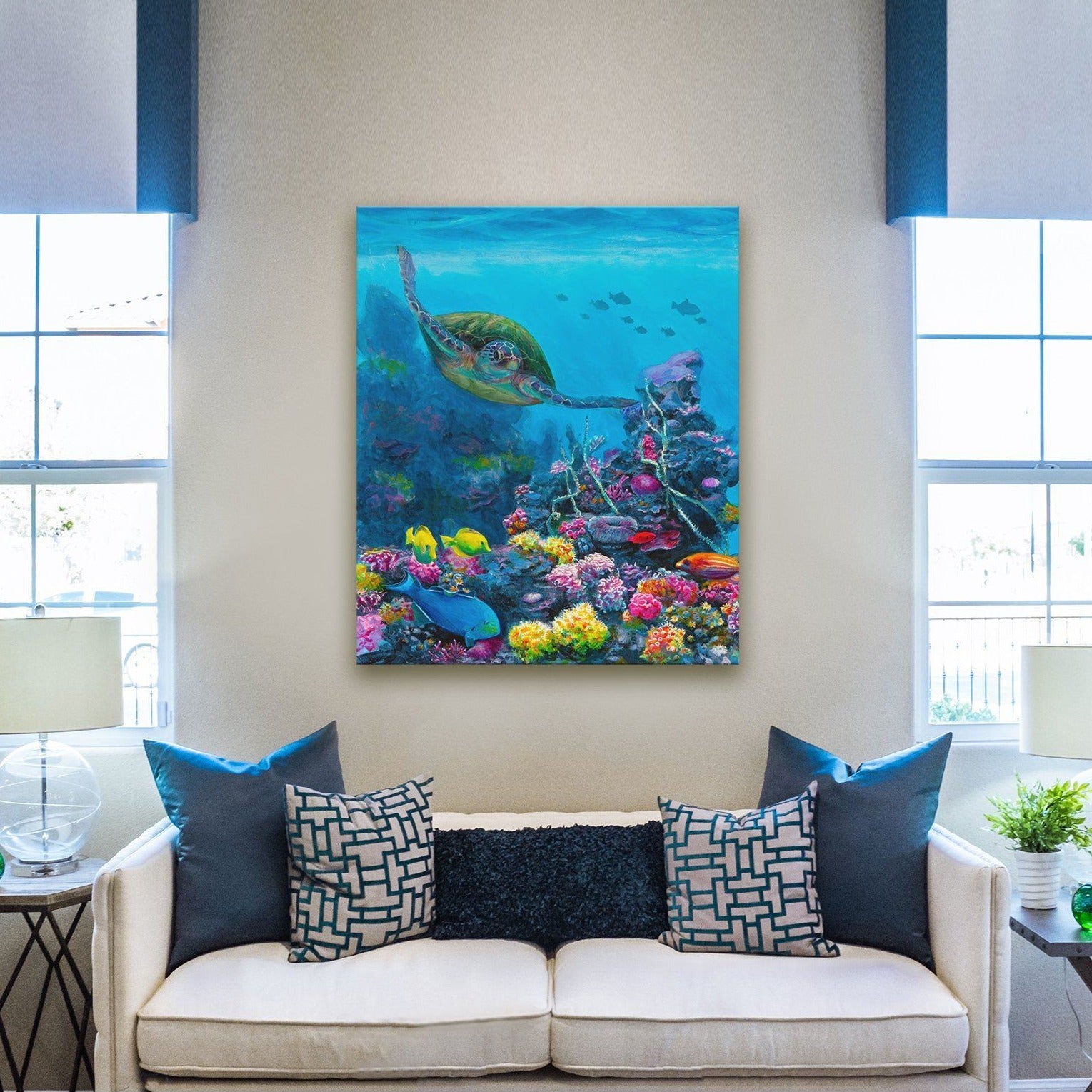 Ocean wall art canvas of green sea turtle swimming through a coral reef with tropical fish hanging on wall above white couch with turquoise blue pillows